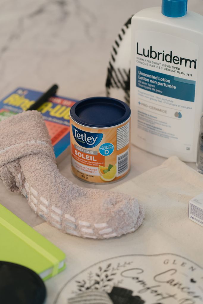 Basket care items including Lubriderm unscented lotion, Tetley herbal tea, soft socks, and a journal laid on the branded tote bag